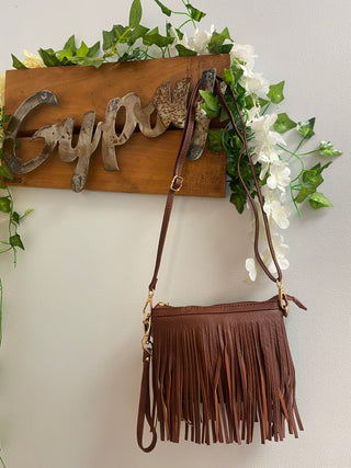 brown fringe crossbody bag hanging from gypsy sign
