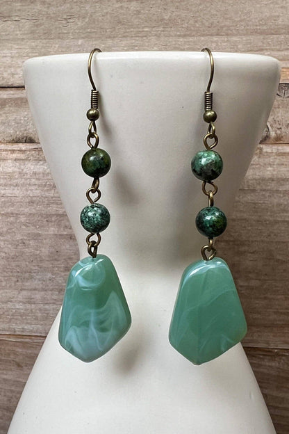 Green stone earrings on a white mannequin bust against a wooden background