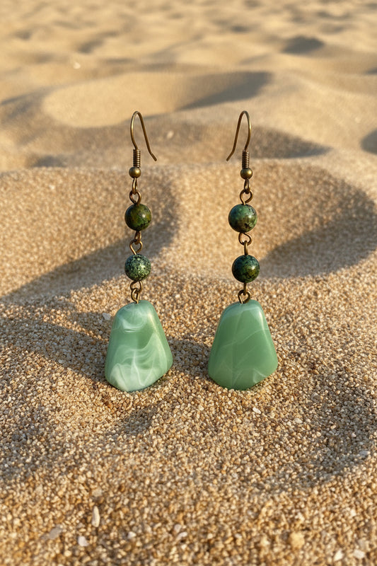 Green stone earrings on a white mannequin bust against a wooden background