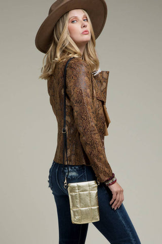 Woman wearing a brown patterned jacket and hat, holding a gold clutch against a neutral background