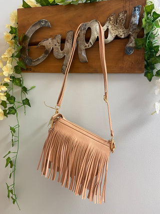 blush fringe crossbody bag hanging from gypsy sign