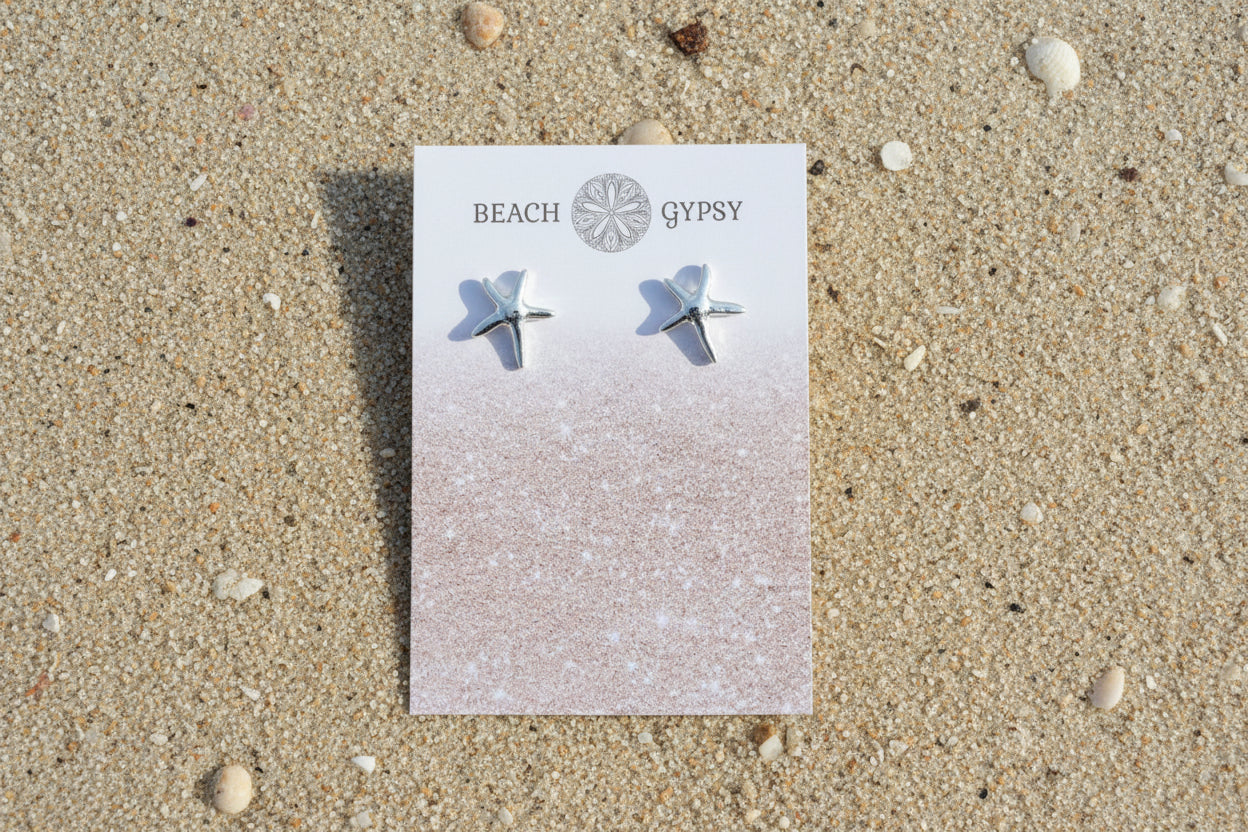 Star-shaped earrings on a Beach Gypsy branded card on a sandy beach