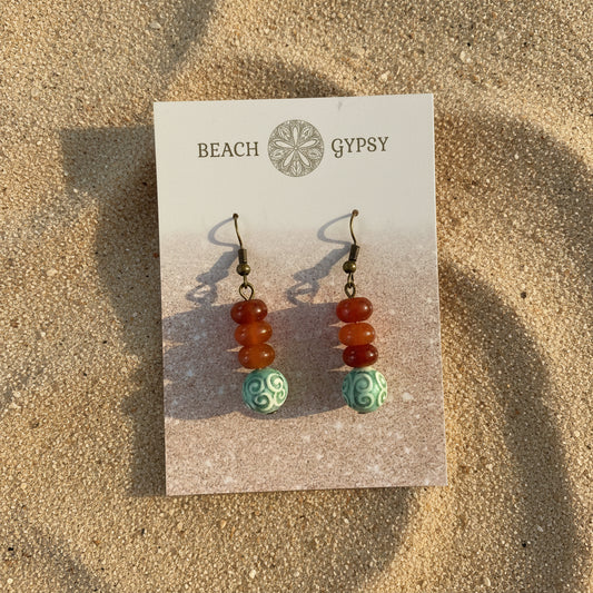 Pair of earrings on a 'Beach Gypsy' branded card on sand