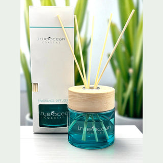 TrueOcean Coastal fragrance diffuser with sticks on a white surface with green plants in the background