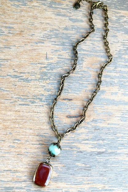 Necklace with a chain, red pendant, and turquoise stone on a wooden surface