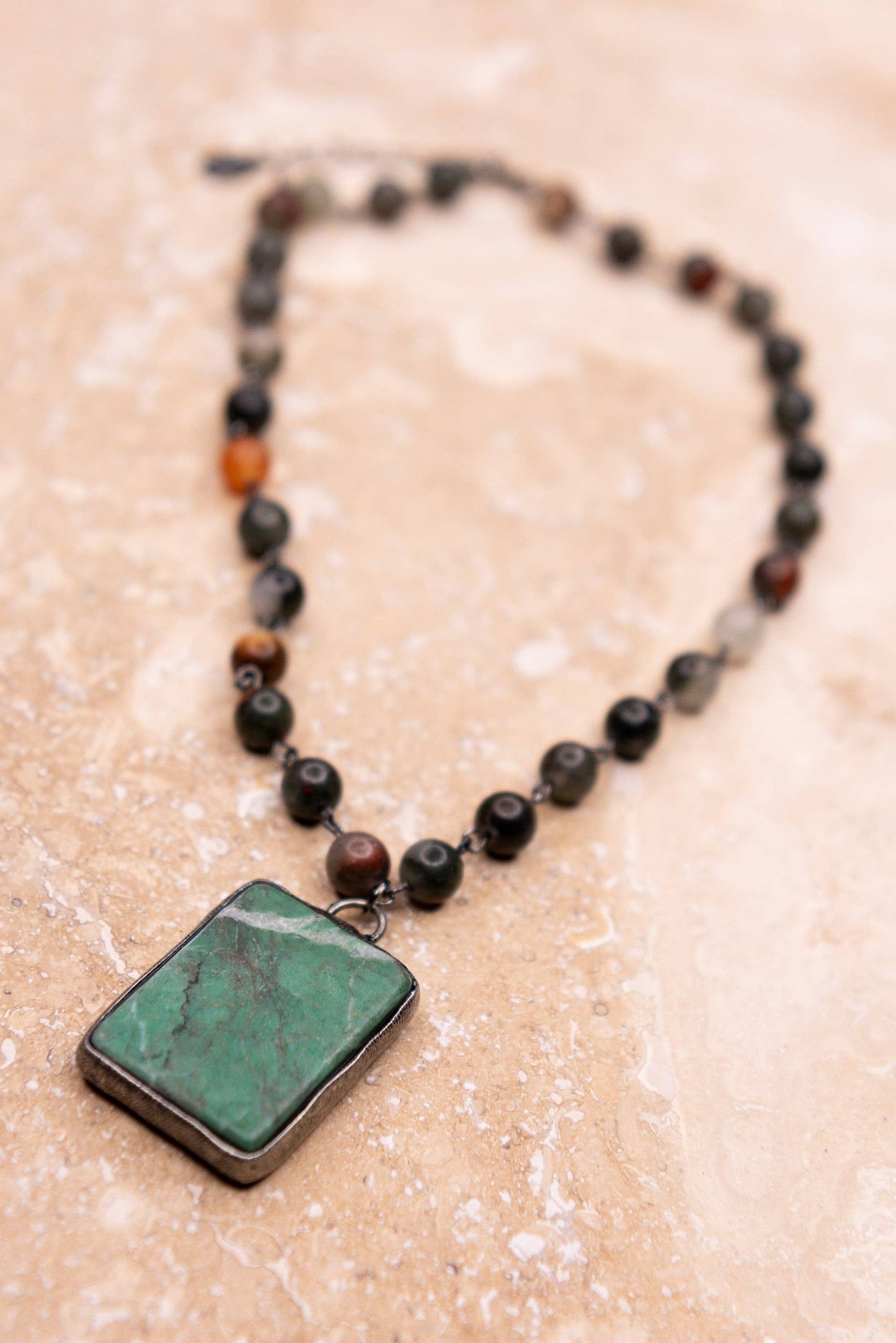 Necklace with a rectangular green pendant on a beige surface