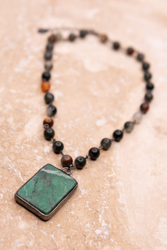 Necklace with a rectangular green pendant on a beige surface