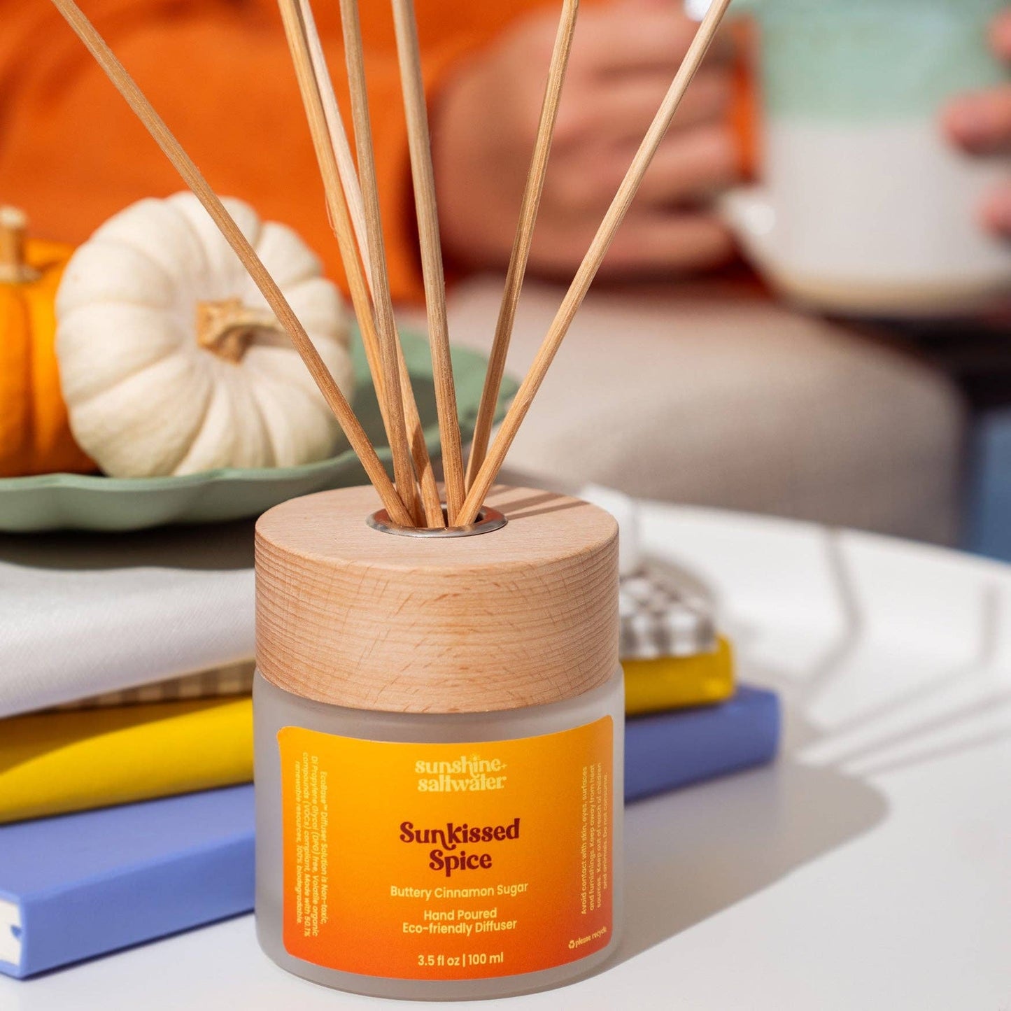 A reed diffuser bottle with a light wood lid and natural reed sticks, labeled 'suncosmic. outdoors.