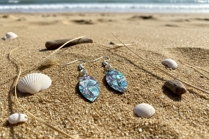Abalone surfboard shaped earrings on sandy background 