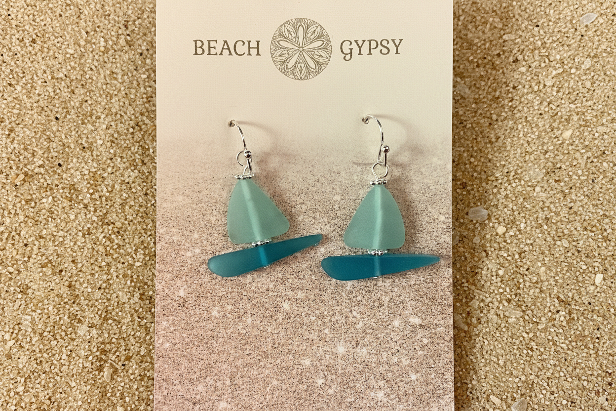 Seaglass sailboat earrings on sand background 
