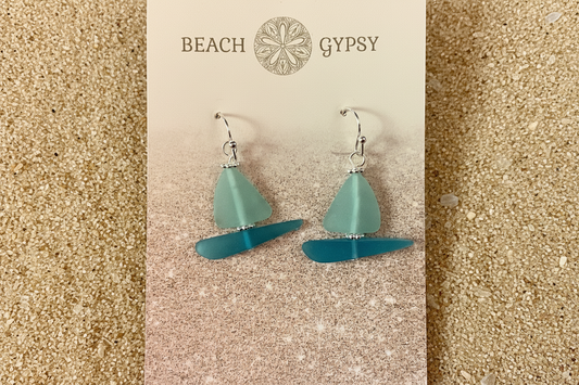 Seaglass sailboat earrings on sand background 