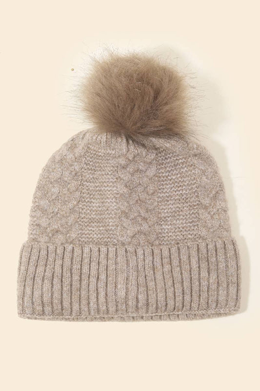 Knitted beanie with a fur pom-pom on a beige background