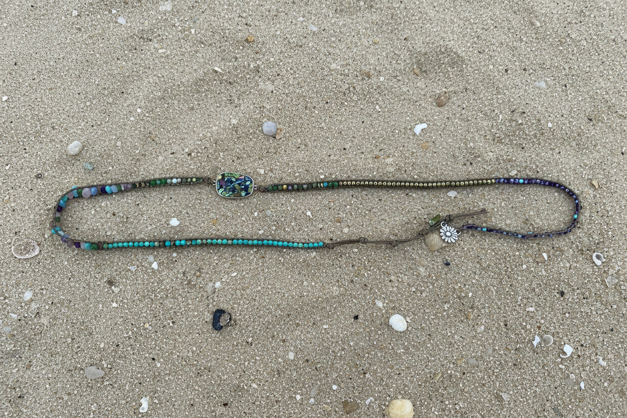 A turquoise and silver beaded necklace laid out on a sand background 