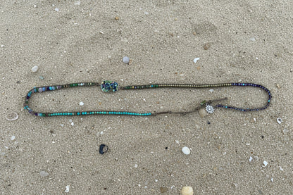 A turquoise and silver beaded necklace laid out on a sand background 
