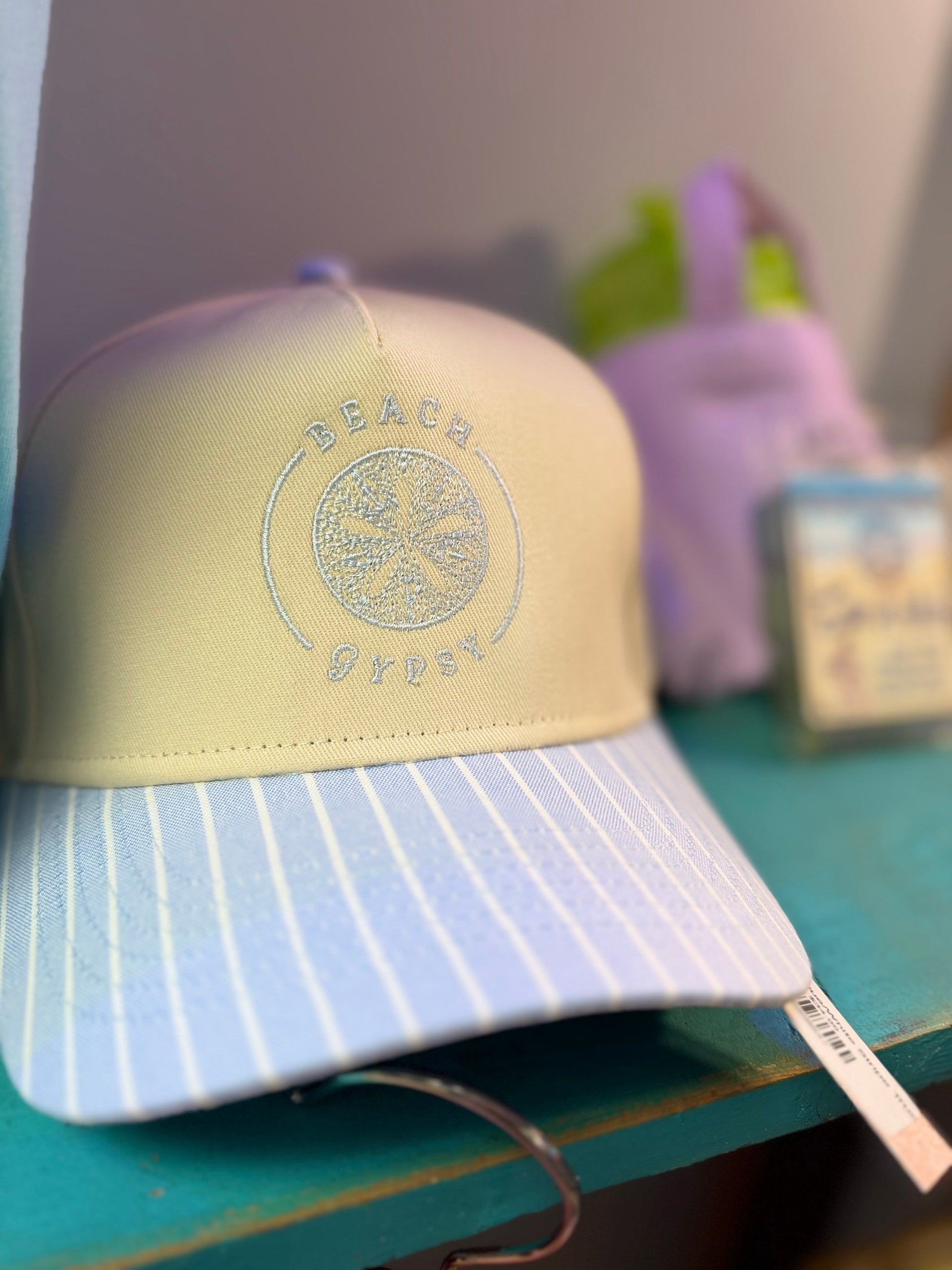 A pastel baseball cap with a pale yellow crown and a light blue brim with thin white pinstripes. The front features an embroidered circular logo with the words 'BEACH GYPSY’