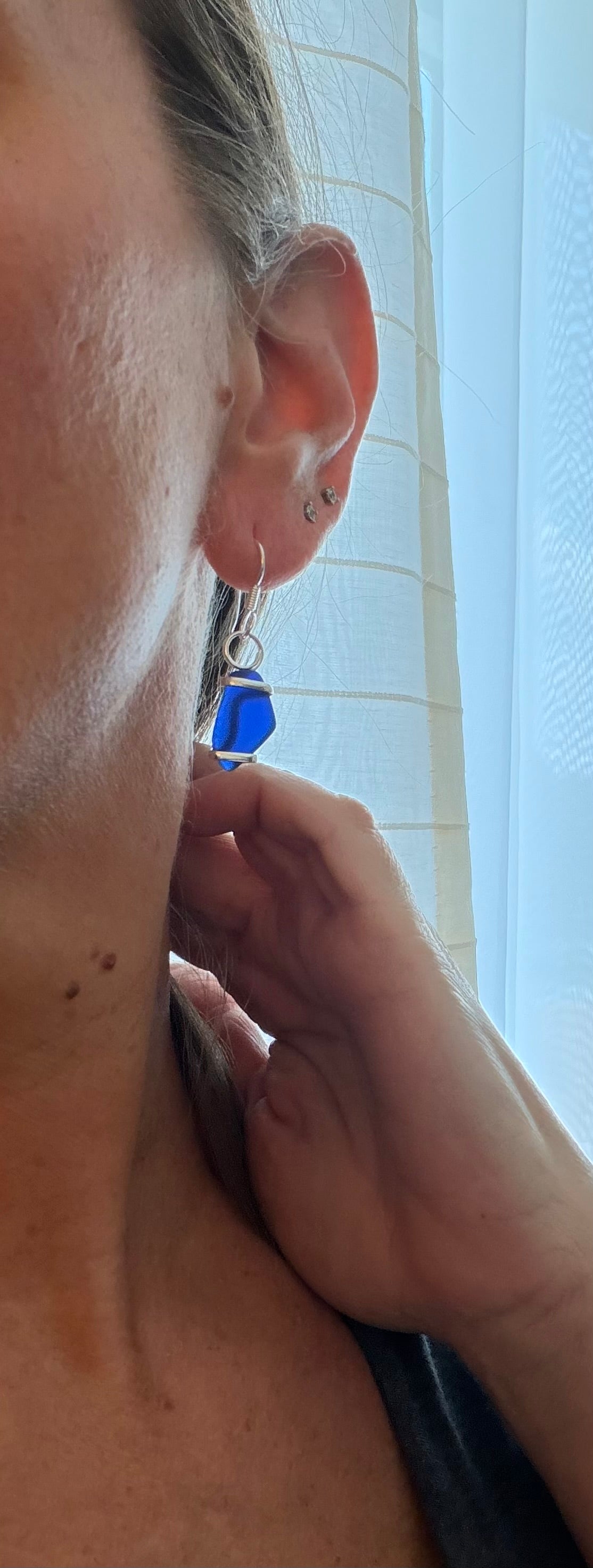 Person wearing a blue sea glass earring with a neutral background