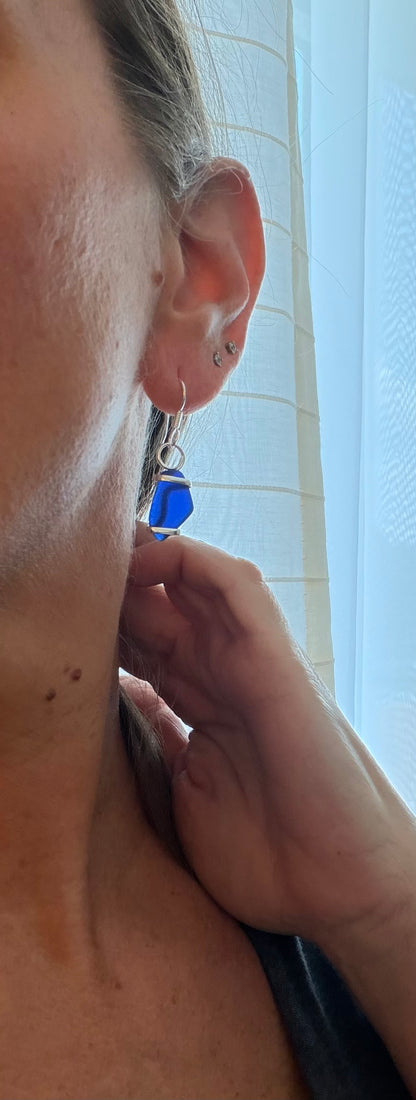 Person wearing a blue sea glass earring with a neutral background