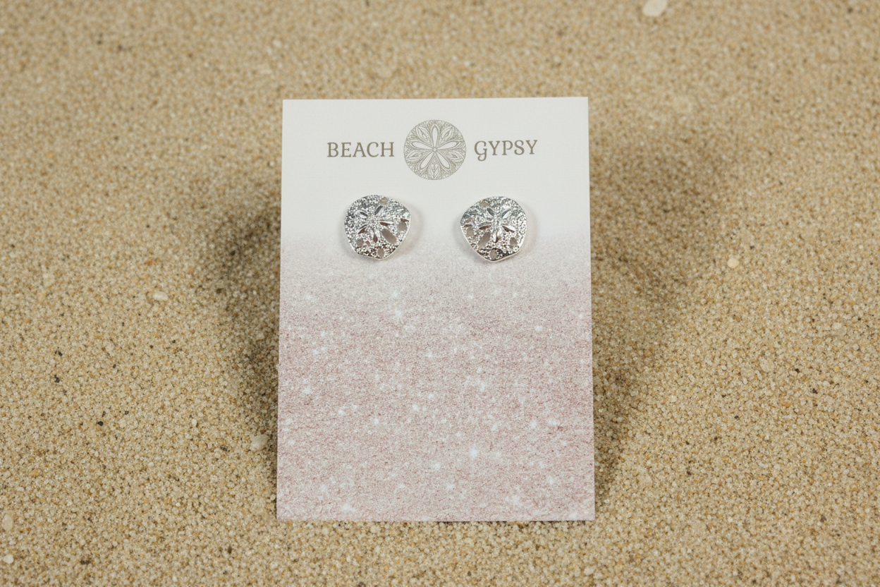 Silver colored sand dollar stud earrings on beach background 