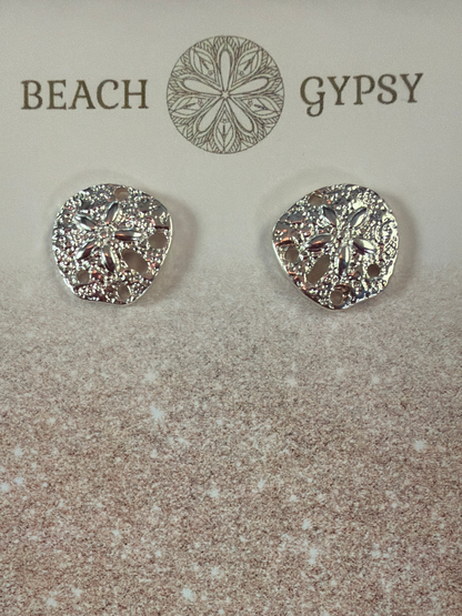 Silver colored sand dollar earrings on a textured surface with 'Gypsy Beach' branding.