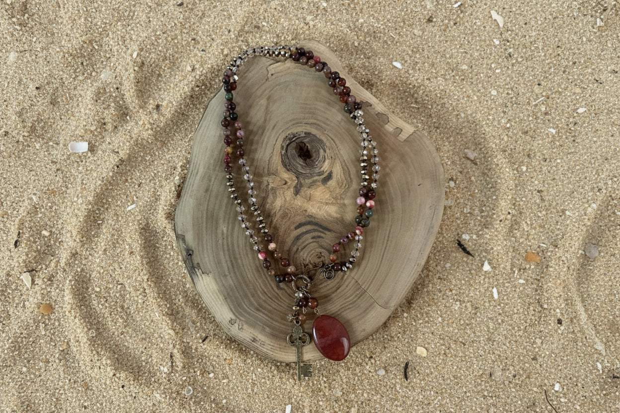 A beaded necklace with red, pink, and metallic beads, featuring a red stone pendant and a vintage-style key charm.