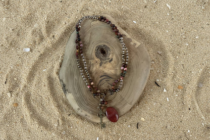 A beaded necklace with red, pink, and metallic beads, featuring a red stone pendant and a vintage-style key charm.