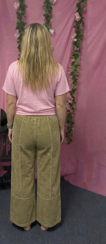 Person wearing a pink shirt and green pants standing in front of a pink curtain with floral decorations.