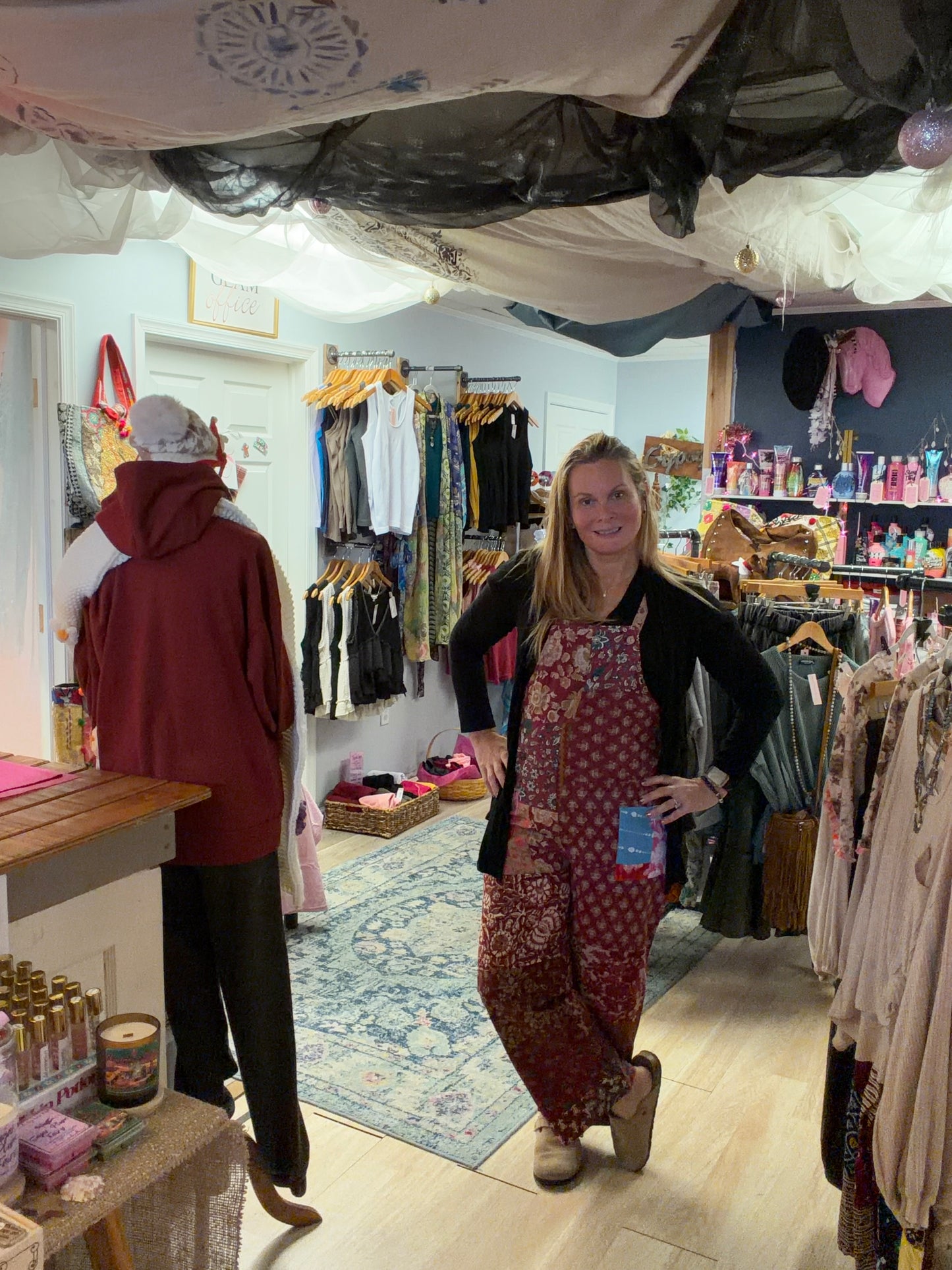 Woman in a store wearing a patchwork jumpsuit surrounded by clothing racks and products.