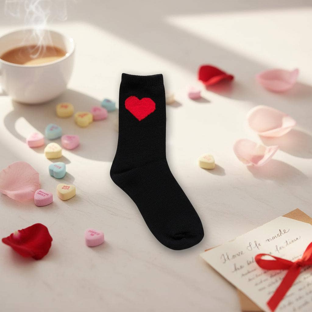 Black sock with a red heart on a surface with coffee, candy hearts, and rose petals.