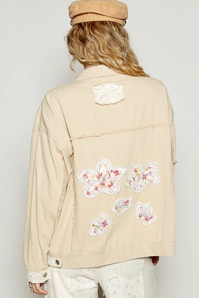 Beige jacket with floral patches worn by a person against a plain background