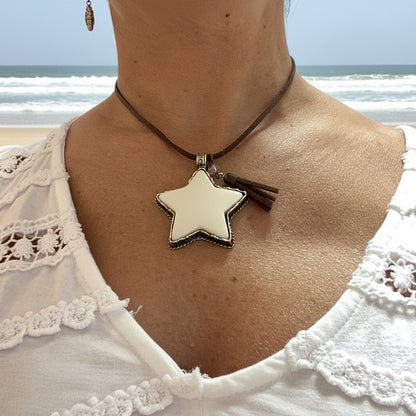 A close-up of a person wearing a bohemian-style necklace with a cream star-shaped pendant on a dark brown cord, paired with a white lace top.