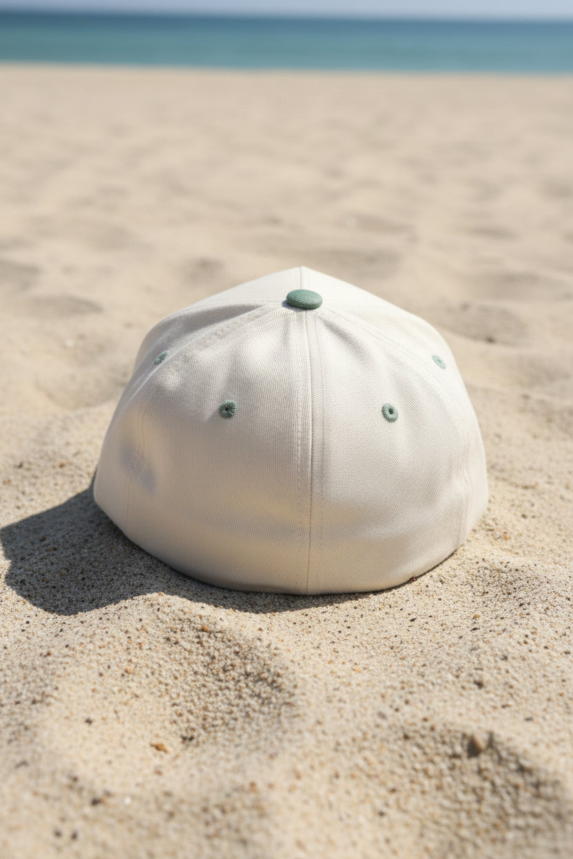 A baseball cap with an off-white crown and an olive green brim, resting on a brown textured surface.