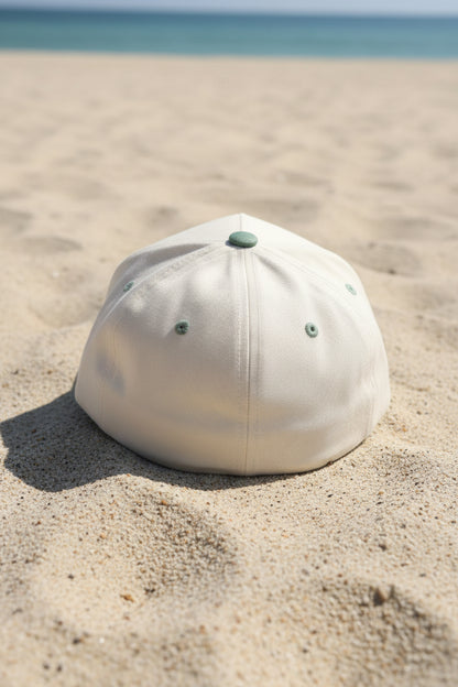 A baseball cap with an off-white crown and an olive green brim, resting on a brown textured surface.