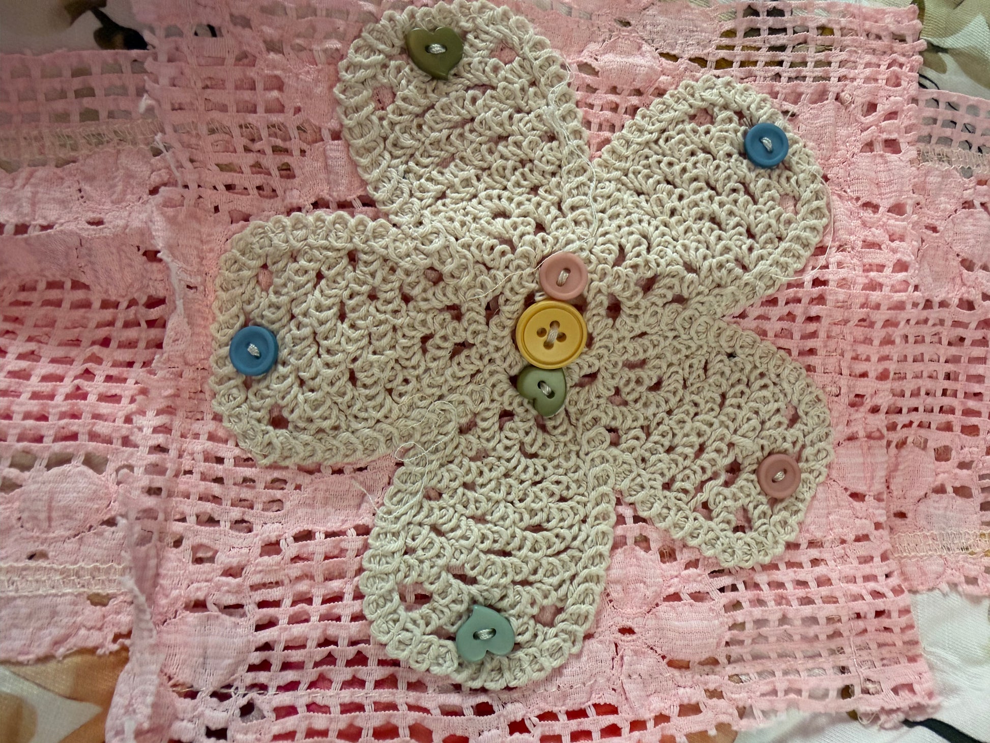 Decorative crochet flower with buttons on a pink lace background