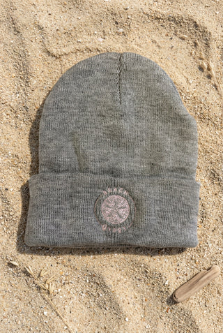 A heather gray knit beanie hat with a folded cuff, featuring a circular embroidered logo on the front that reads 'BEACH GYPSY’
