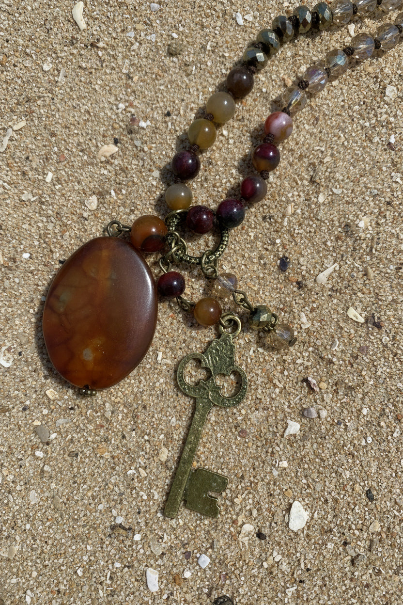 A beaded necklace with a large oval amber-brown stone pendant and an antique-style metal key charm,
