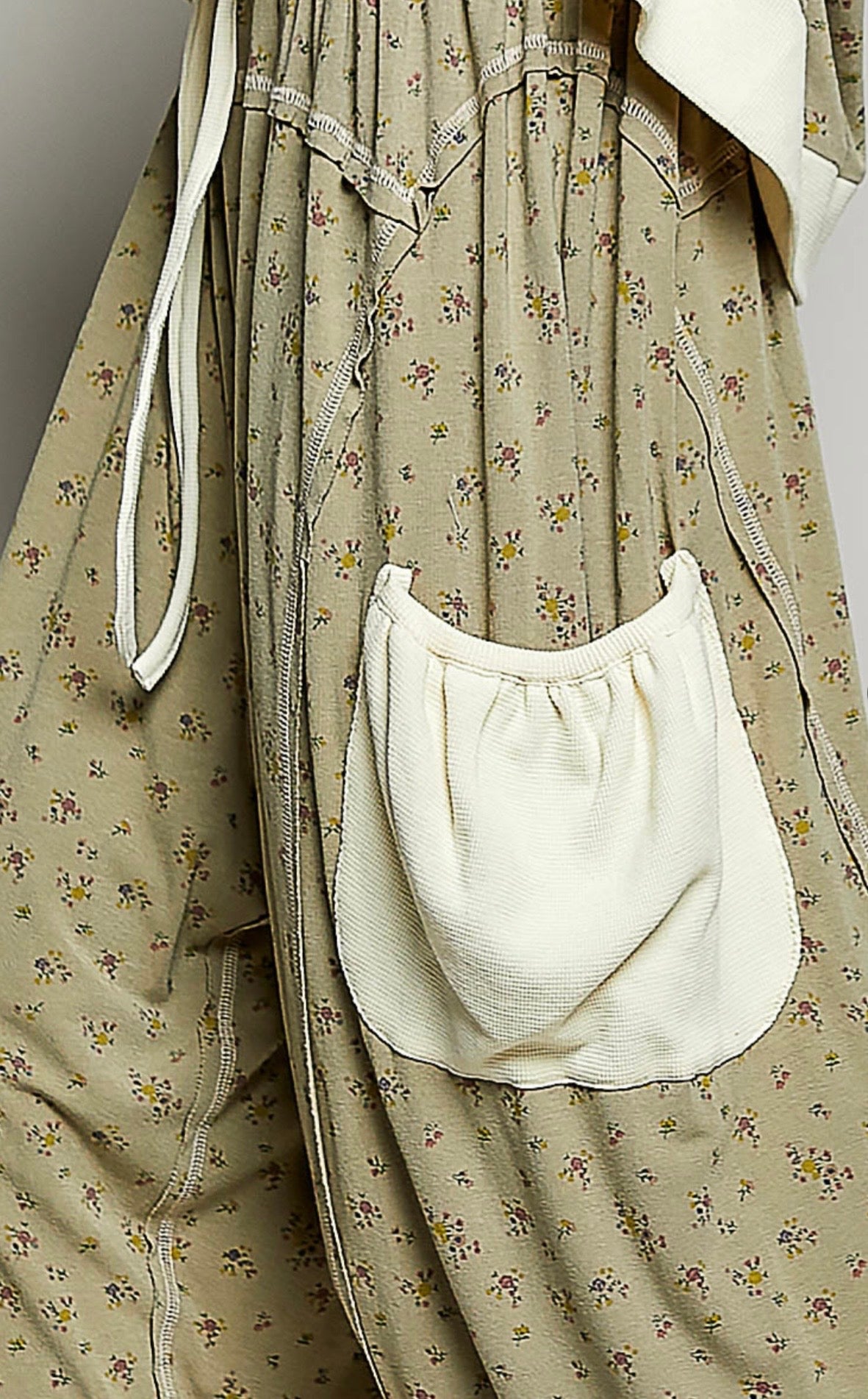 Close up of fabric on Woman wearing flowing sage colored ditzy flower print pants with cream patch pockets