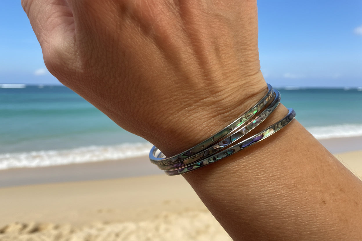 Close-up of a wrist wearing multiple metallic bracelets on a beach background