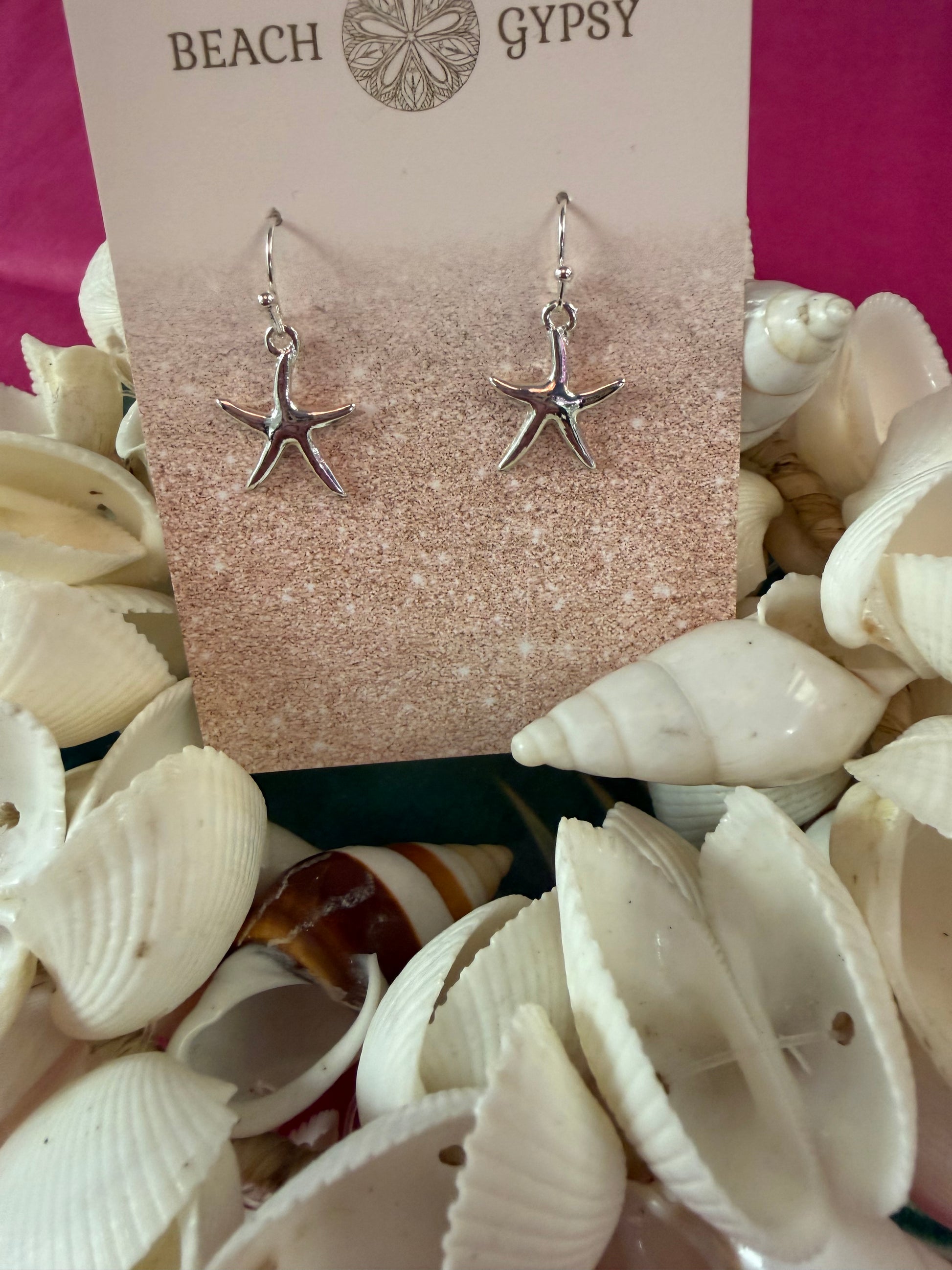 Starfish-shaped earrings on a 'Beach Gypsy' card surrounded by seashells.