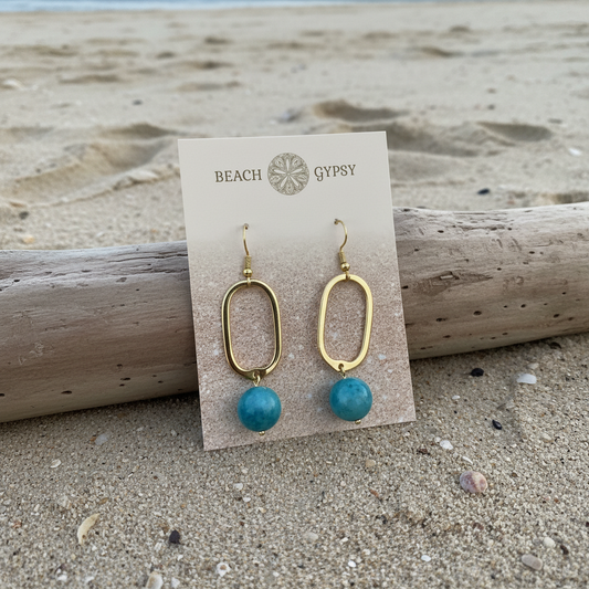 Blue sky stone earrings on gold dangle rectangular hook earring on beach background 