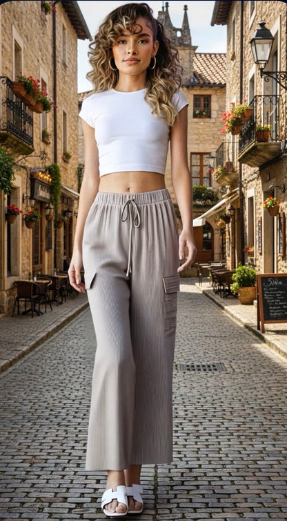 Woman in white top and beige pants standing on a cobblestone street in an old town.