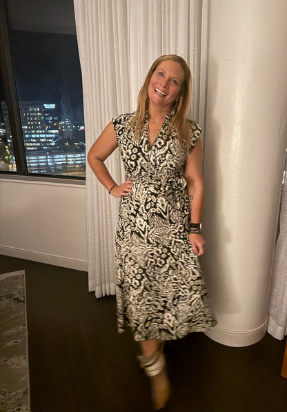 Woman in a patterned dress standing in a room with a window view of a cityscape.
