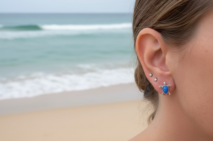 Close-up of a person wearing a blue gemstone earring with a turtle design.