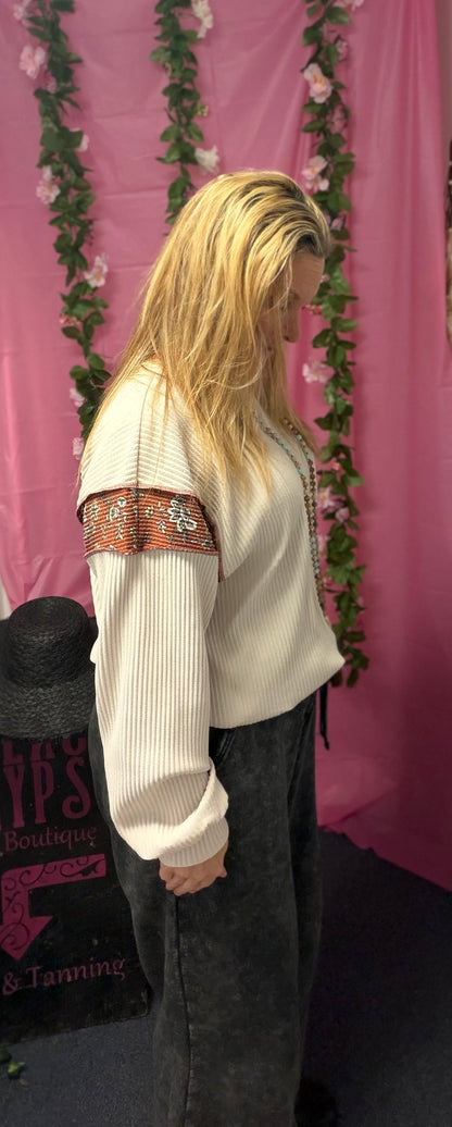 Person wearing a white sweater with colorful patterns in front of a pink curtain with floral decorations.