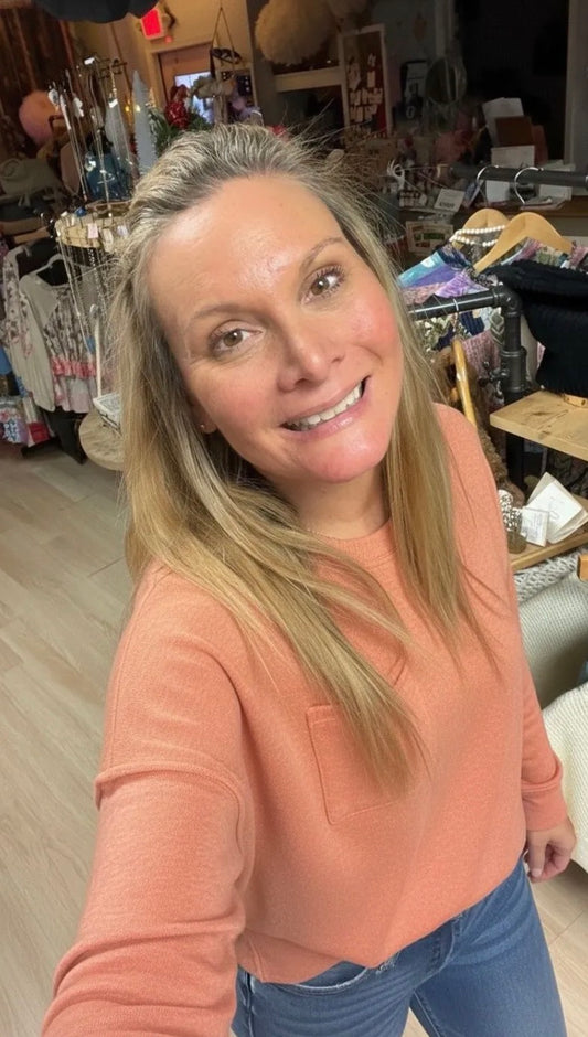 Woman in a peach-colored shirt standing in a store with various items in the background