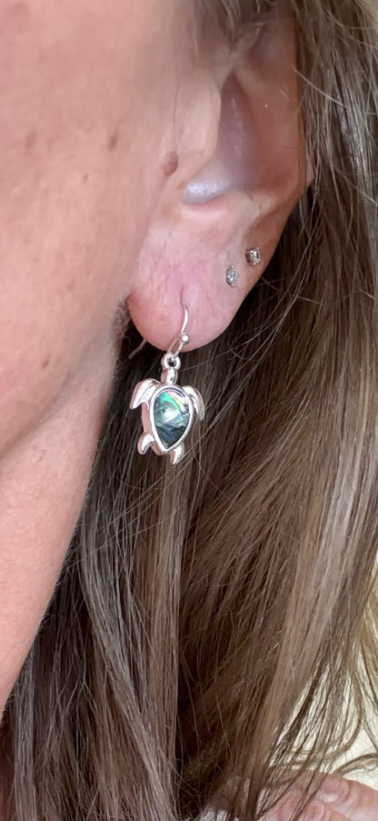 Close-up of a person wearing a turtle-shaped earring with a green gemstone.