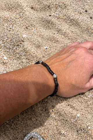 A close-up of a person's wrist wearing a dark beaded bracelet with silver-toned spacer beads
