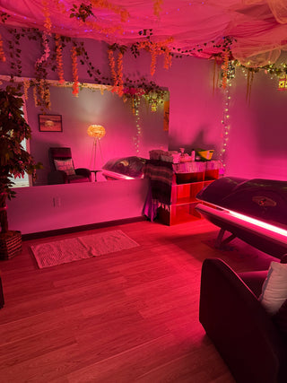 Pink-lit room with decorative lights and plants, featuring a bed and lamp.
