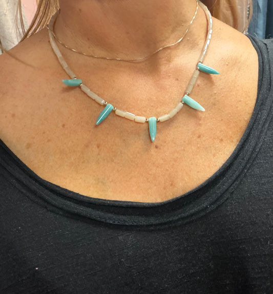 Necklace with turquoise spikes and beige beads worn by a person
