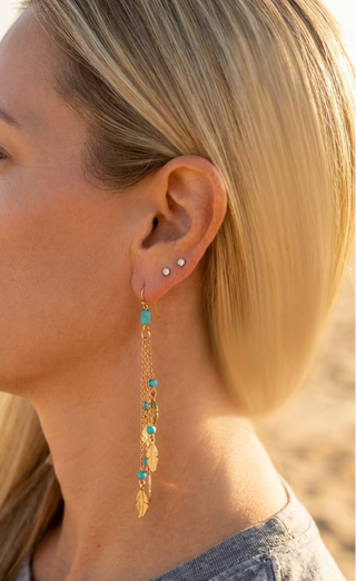 Woman at the beach wearing Turquoise Beaded Feather Chain Earrings, showing the long cascading drop