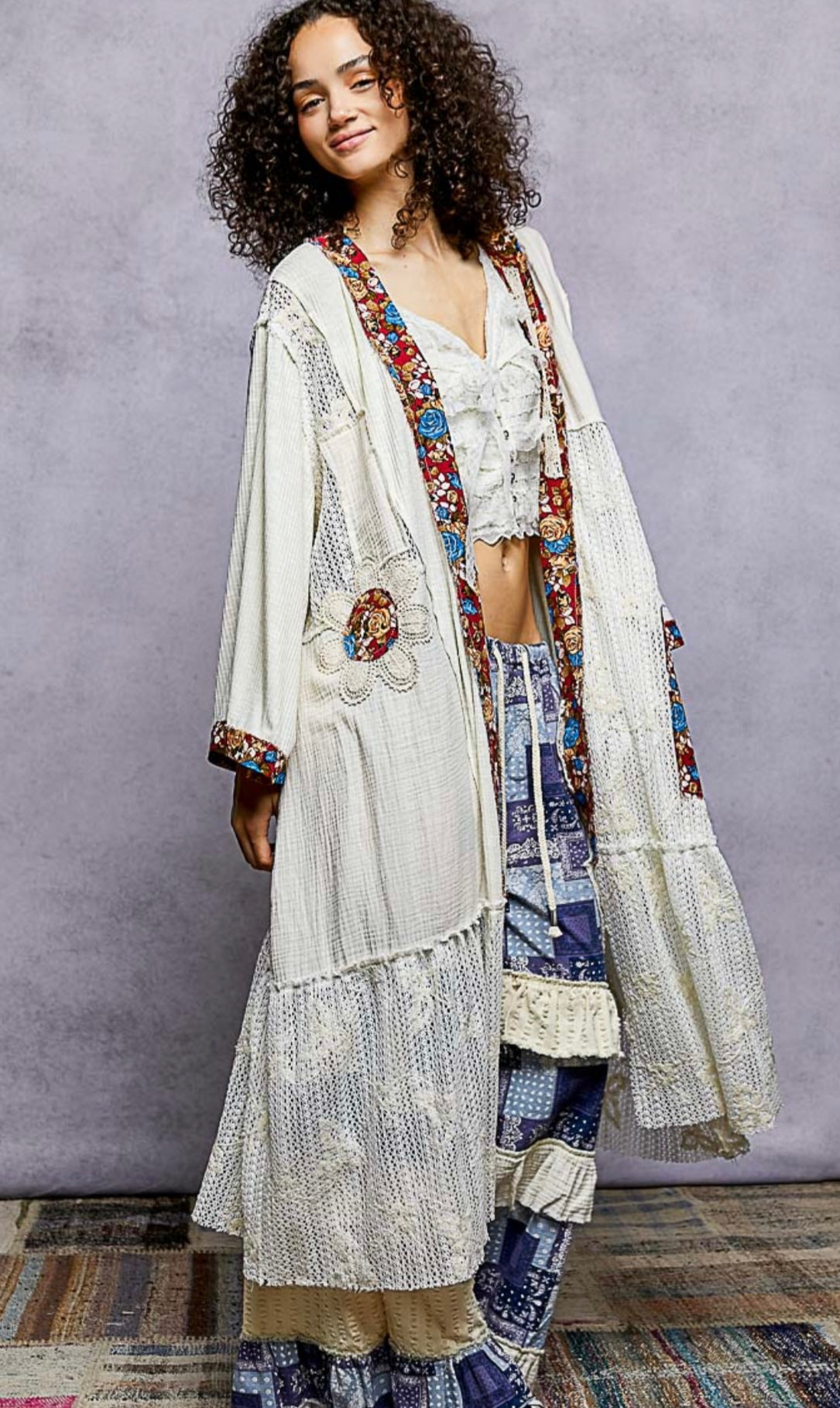 Woman wearing a bohemian-style outfit with a long, patterned jacket and layered skirt against a plain background.